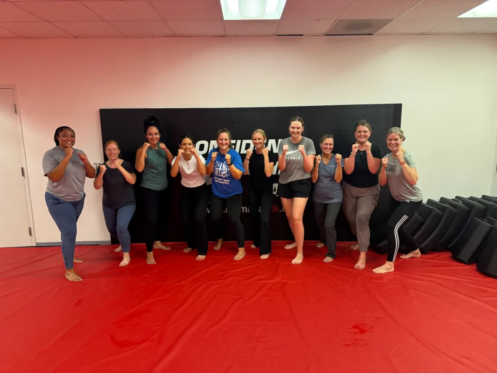 Self Defense Women class posing with raised fists on the training mats at Krav Maga CDK.