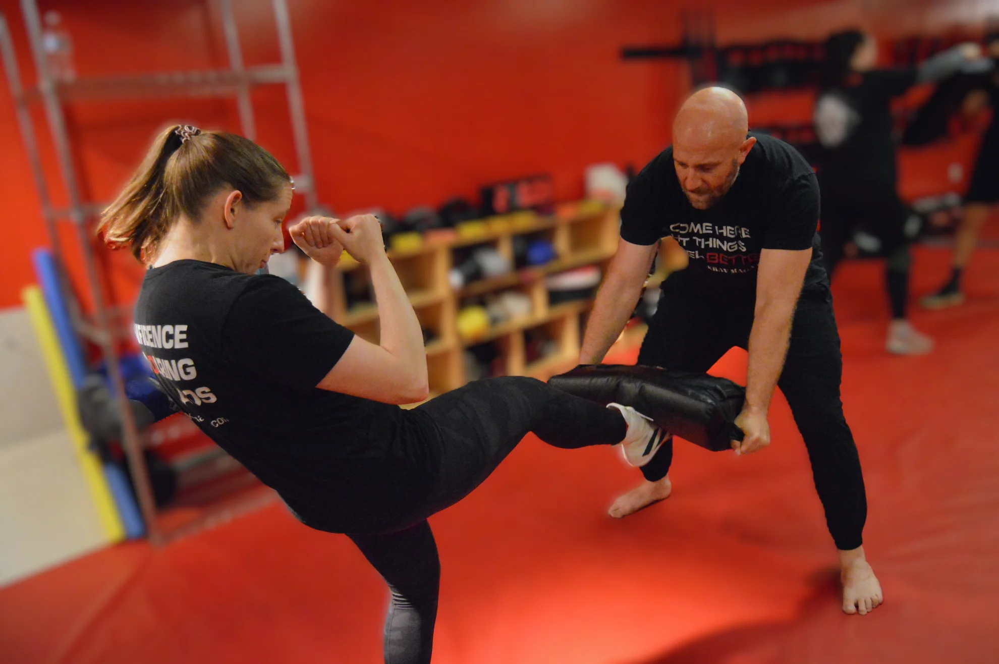 Woman practicing a powerful front kick on a training pad during a Krav Maga class in Bethesda, Maryland.
